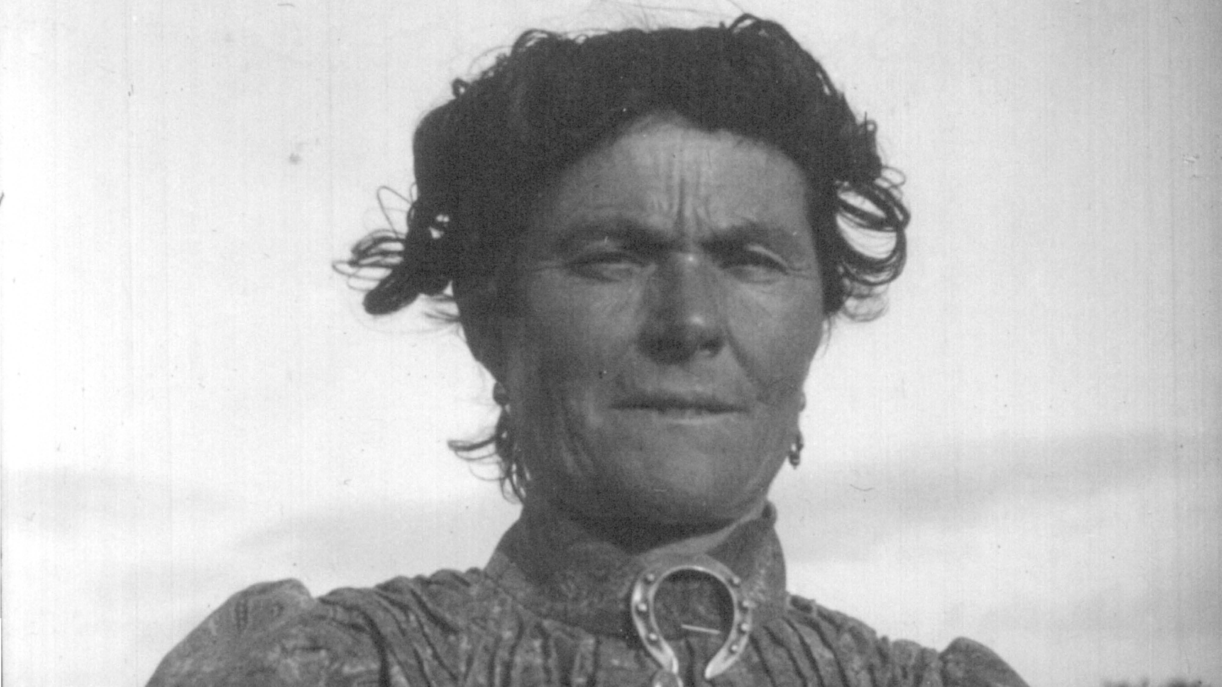 historical image of female, smartly dressed with a horse-shoe shaped broach under her chin